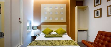 Une chambre d’hôtel comprenant un lit, une chaise, un bureau avec une lampe et un luminaire fixé au mur.