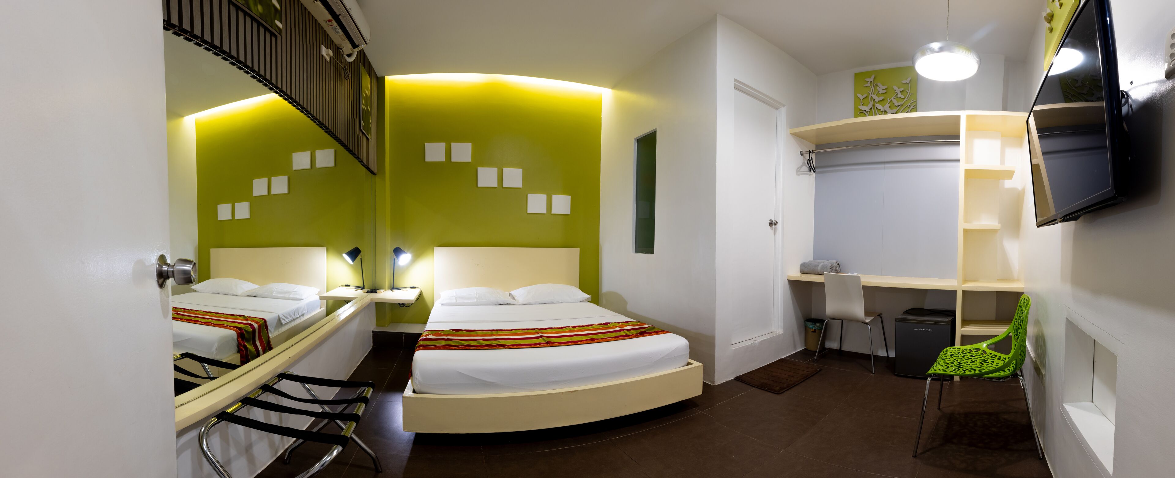 A hotel room with two beds, a desk, a chair, a TV, and a small trash bin.