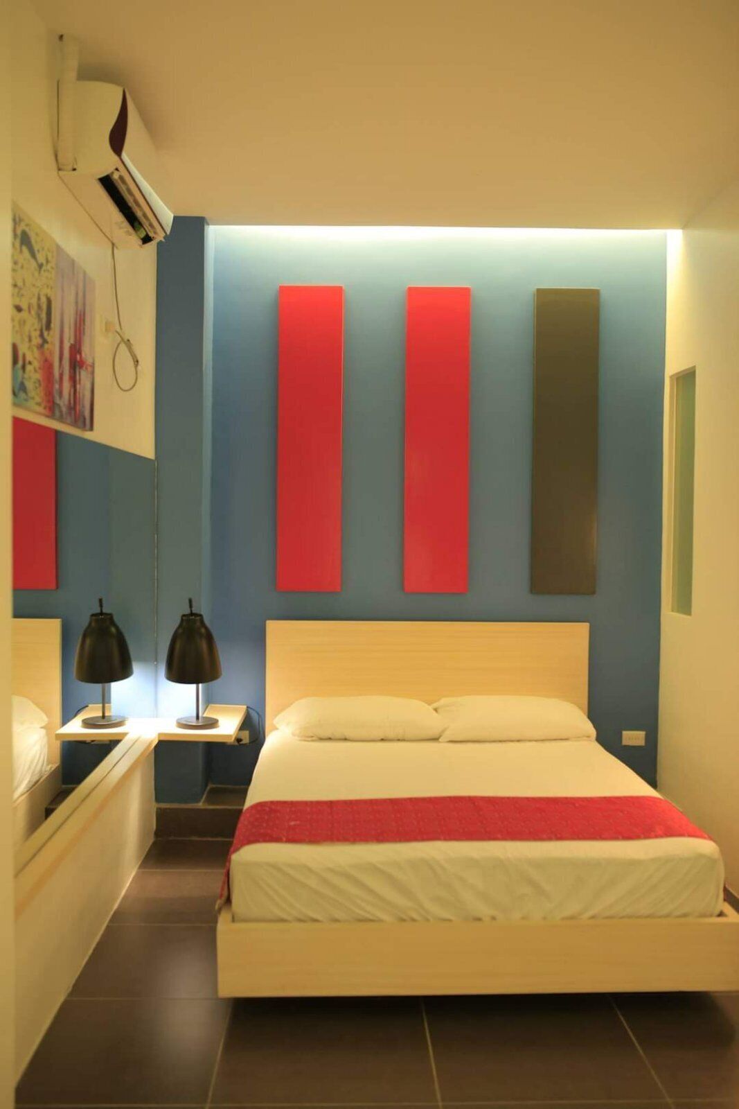A hotel room with a bed, bedside tables, and a wall-mounted air conditioner.