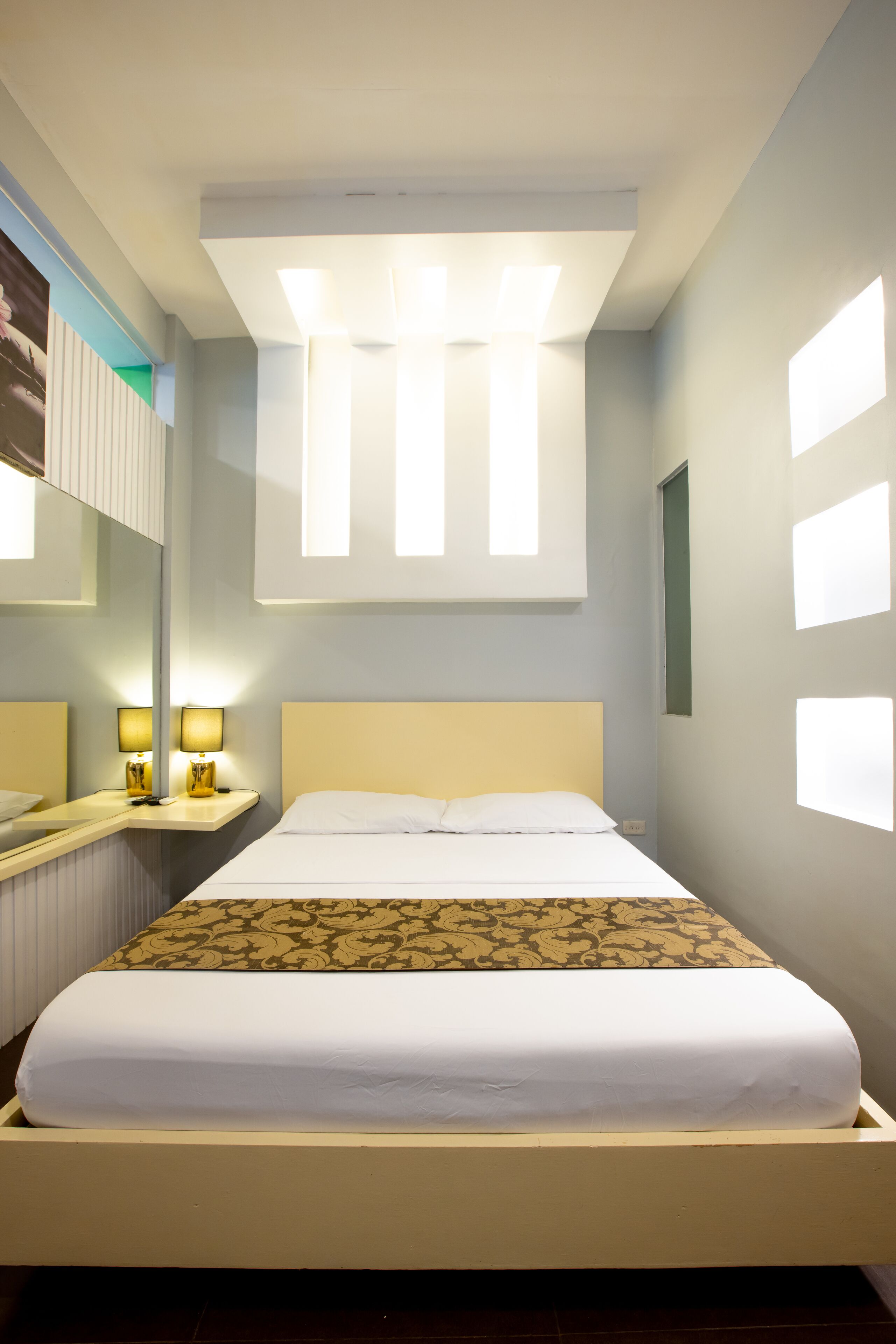 Una cama bien hecha con un edredón estampado, una mesita de noche con lámparas y un espejo grande en la pared.