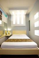 Una cama bien hecha con un edredón estampado, una mesita de noche con lámparas y un espejo grande en la pared.
