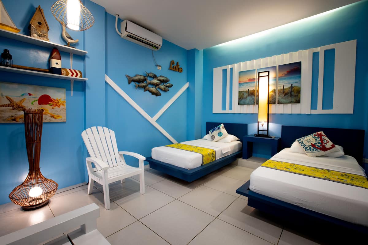 A room with two beds, a chair, and a shelf with decorative items.