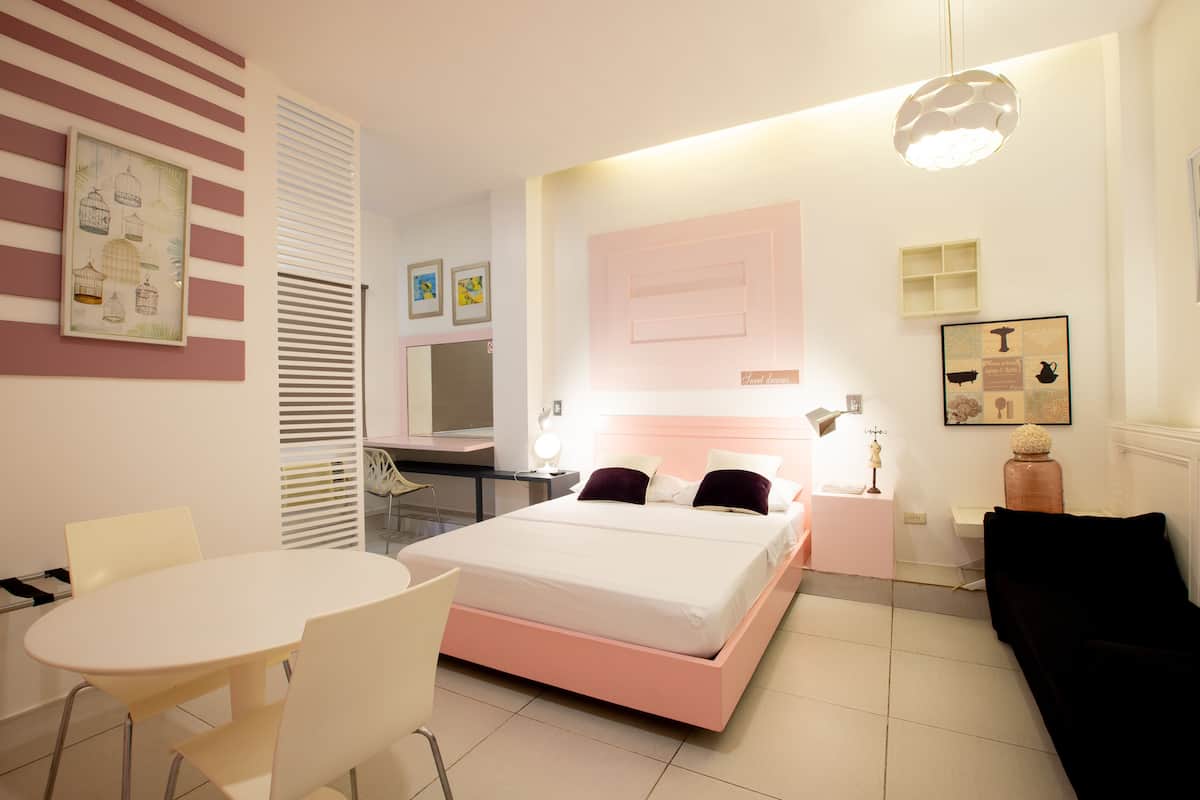A modern bedroom with a bed, bedside table, lamp, and a desk with a chair.