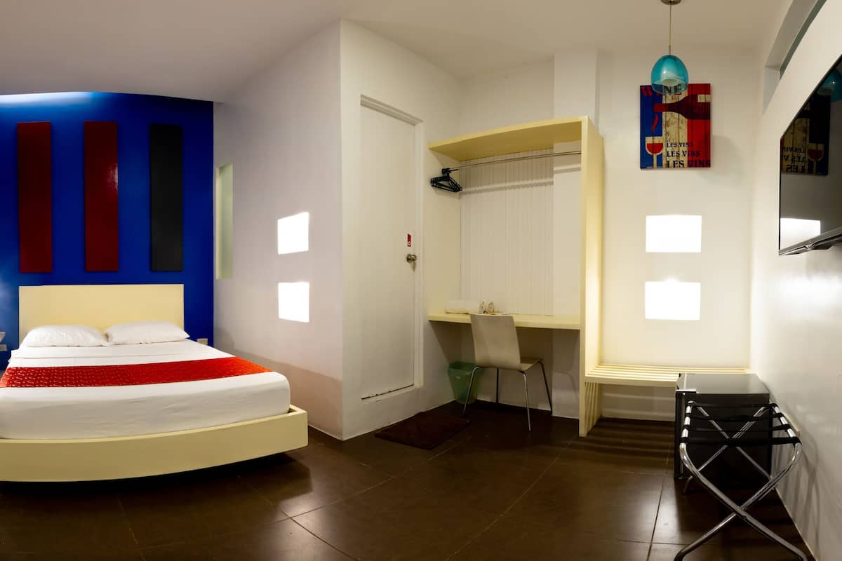 A modern hotel room with a bed, a desk, a chair, a TV, and a wardrobe.