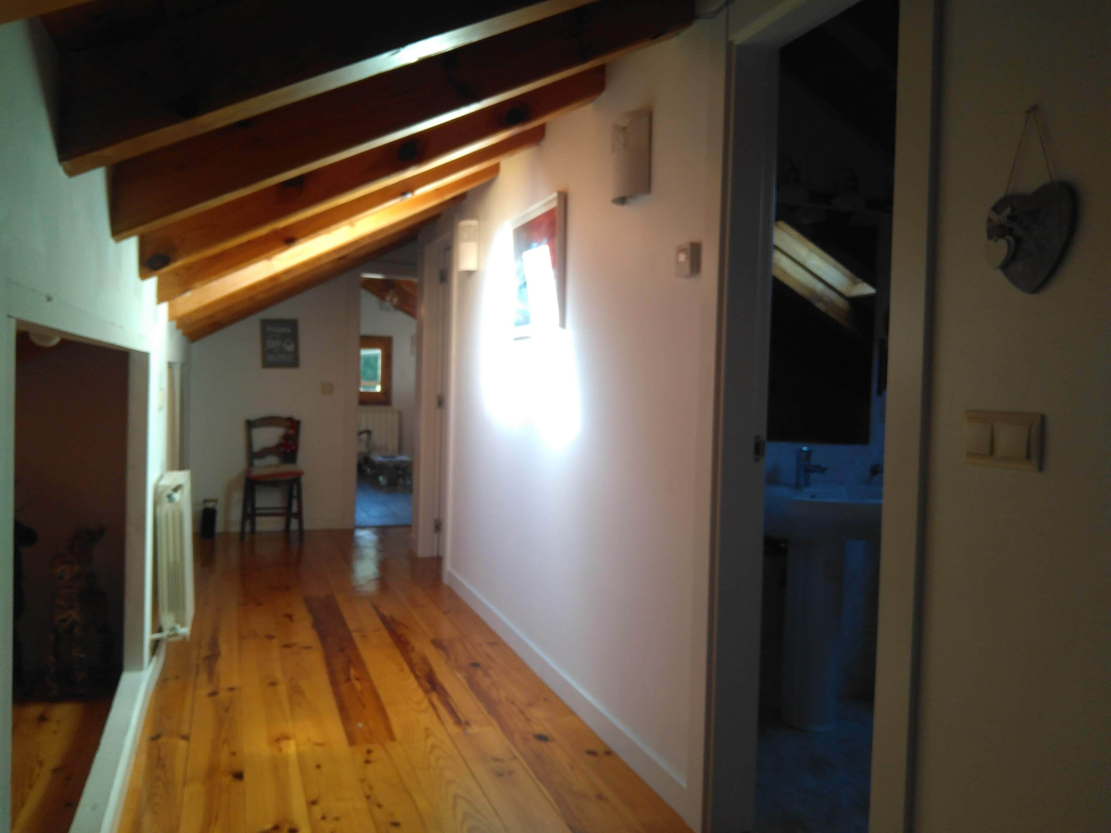 Un estrecho pasillo con piso de madera, techo inclinado y una puerta que da a un baño.