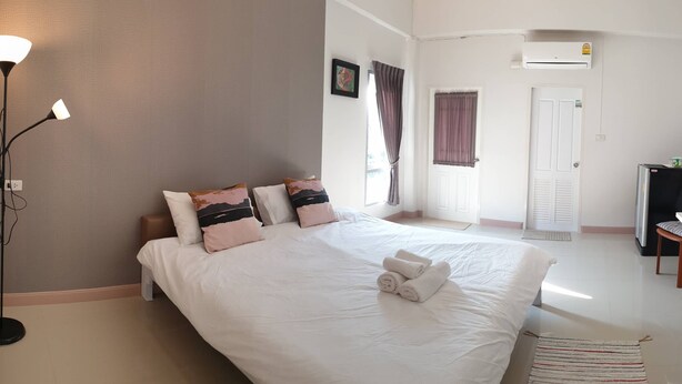A bedroom with a bed, bedside lamps, a desk, and an air conditioning unit. - Prinya House (Chonburi)
