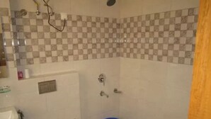 A bathroom with a checkered tile backsplash, a white toilet, a blue bucket, and a shower area.