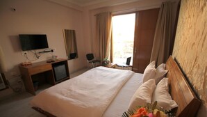 A hotel room with a large bed, a desk with a television, and a window with curtains.