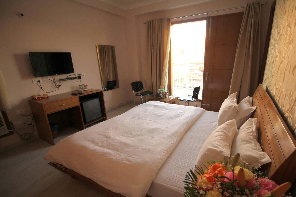 Una habitación de hotel con una cama grande, un escritorio con televisor y una ventana con cortinas.