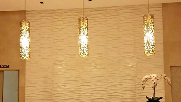 Un mostrador de recepción con una pared texturizada y tres lámparas colgantes.