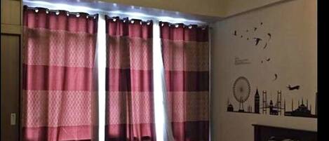 A bedroom with a bed, curtains, a wall clock, and a ceiling light fixture.