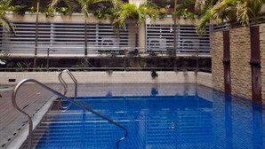 Una piscina con una escalera metálica, rodeada por un suelo de baldosas y un muro de ladrillo.