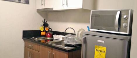 A compact kitchen with a microwave, a refrigerator, and wooden cabinets.