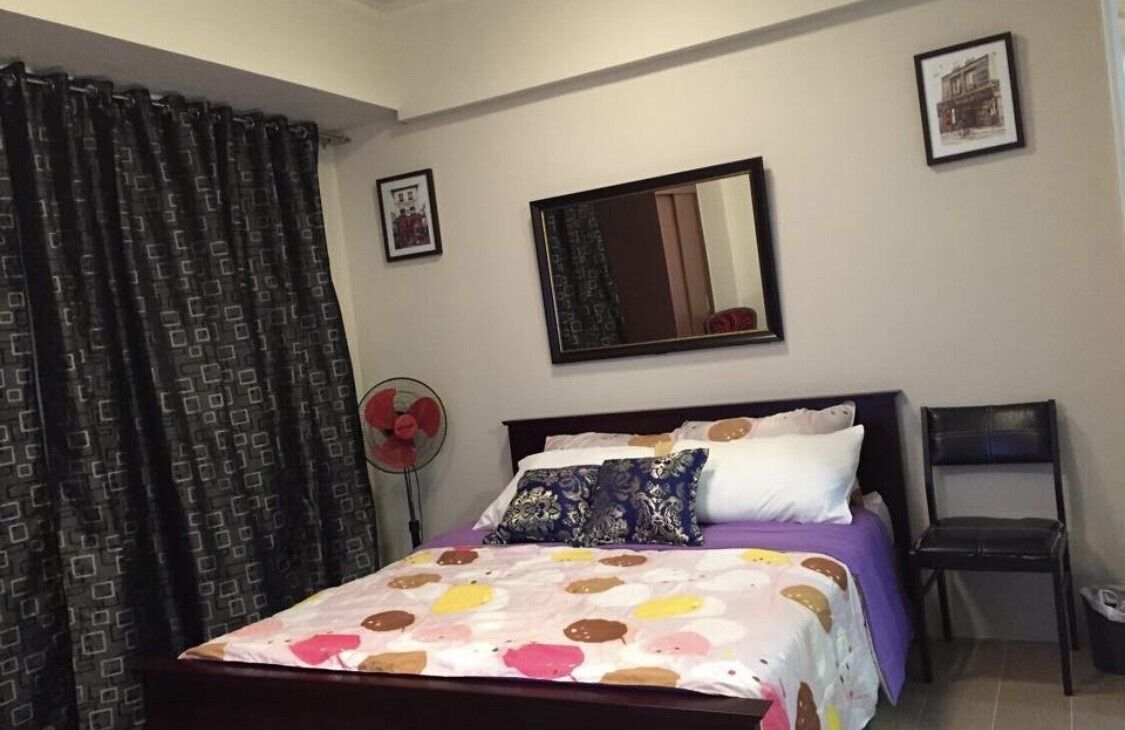 Un dormitorio con cama, una silla, un ventilador y un espejo en la pared.