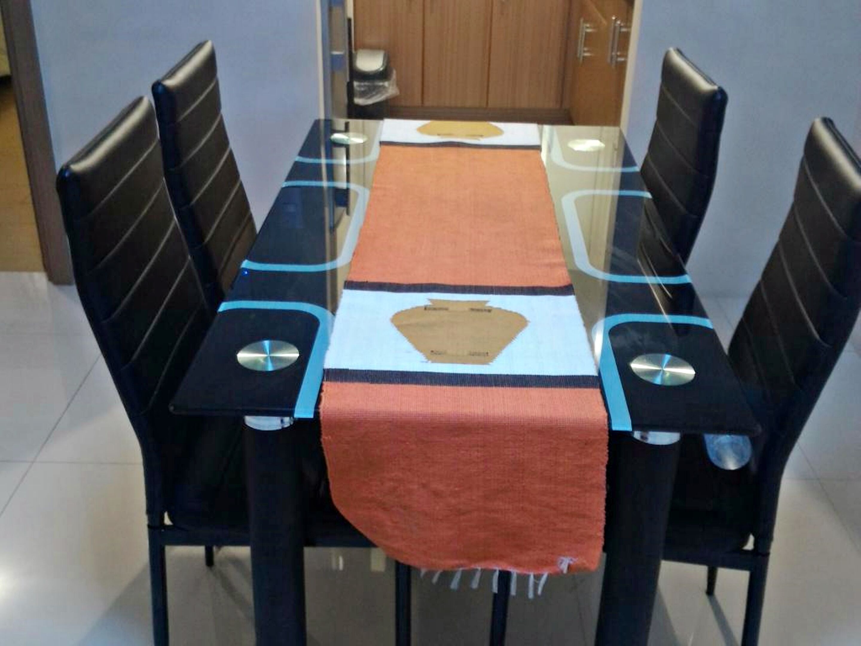 Een eethoek met een tafel met een glazen blad, zwarte stoelen met blauwe accenten en een rode tafelkleed.
