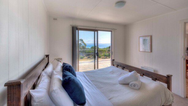 Ein Schlafzimmer mit einem großen Bett, Meerblick durch eine Schiebetür und einem gerahmten Bild an der Wand.