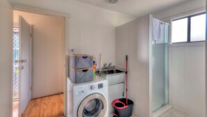 Ein kleiner Waschraum mit Waschmaschine, Spüle, einem Mop und einer Duschkabine aus Glas.