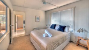 Ein Schlafzimmer mit einem Bett, einem Fenster mit Jalousien, einer Nachttischlampe und einer Tür zu einem anderen Raum.