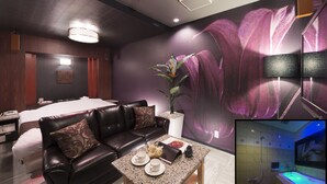 Una habitación de hotel moderna con una cama grande, un sofá de cuero, una mesa de centro y un televisor montado en la pared.