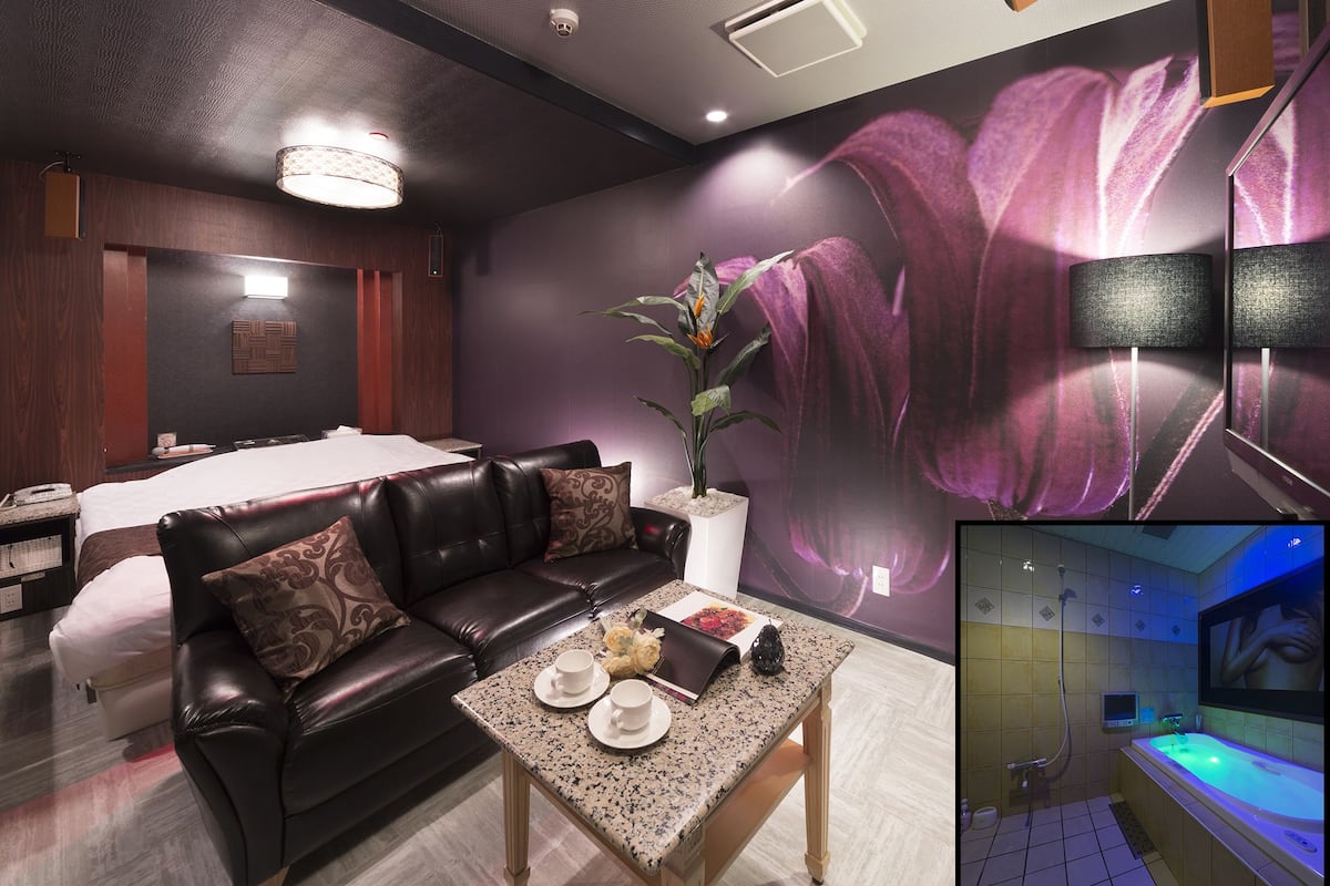 A modern hotel room with a large bed, a leather sofa, a coffee table, and a wall-mounted TV.