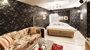 A bedroom with a floral-patterned sofa, a bed with a white mattress, a tray with candles and a rose, and a red rug. - Hotel & SPA Island Adult Only (Toyota)