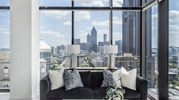 A modern living room with a black sofa, white coffee table, and a large window offering a city view. - Vue Spectaculaire Penthouse (Atlanta)