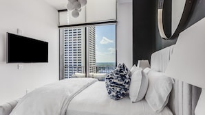 A modern bedroom with a large bed, a flat-screen TV, and a balcony with a city view. - Vue Spectaculaire Penthouse (Atlanta)