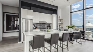 A modern kitchen with white cabinetry, a large island, and a dining area with bar stools. - Vue Spectaculaire Penthouse (Atlanta)