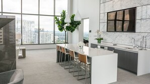 A modern kitchen with a large island, bar stools, a marble backsplash, and a city view through large windows.