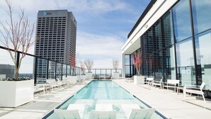 Piscina no terraço com indicador de profundidade de 1,8 metros, rodeada por espreguiçadeiras brancas e edifícios modernos ao fundo.