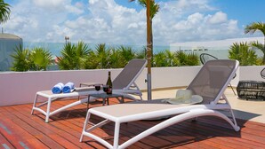 Una terraza en la azotea con dos sillones blancos, una mesa con bebidas y un paraguas grande.