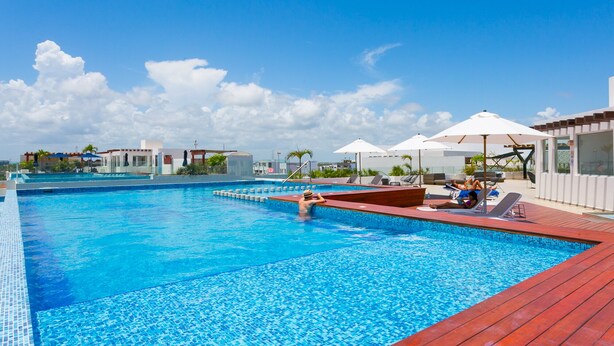 Una piscina con solárium de baldosas, sillas de descanso y sombrillas.