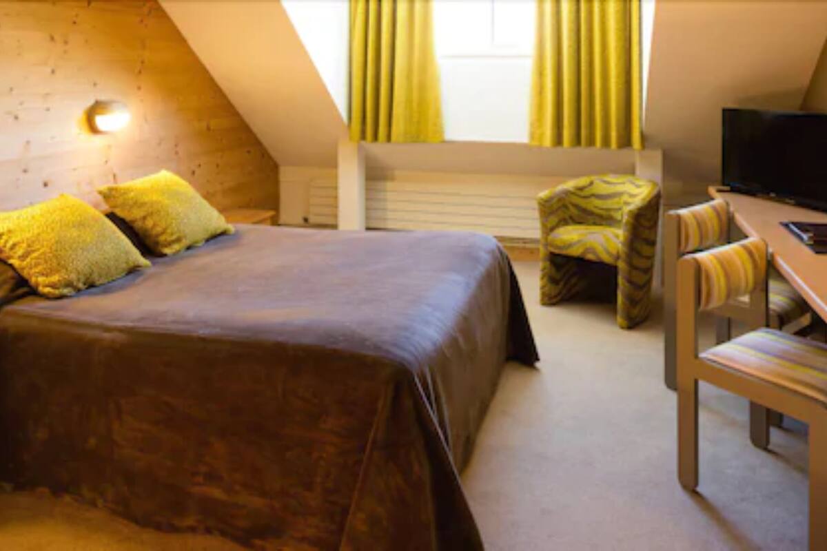 Une chambre à coucher avec un lit, un bureau et une chaise, une télévision et une fenêtre avec des rideaux.