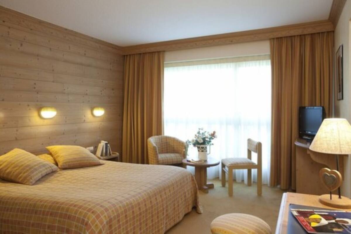 Une chambre d’hôtel avec un grand lit, deux chaises, une petite table, un téléviseur et une lampe.