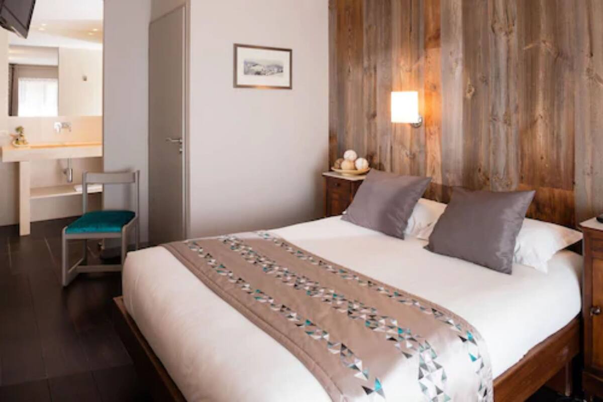 Une chambre d’hôtel comprenant un lit, une tête de lit en bois, une table de chevet, une commode, une chaise, un bureau et un miroir.