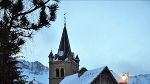 Une église enneigée, avec un clocher, et un bonhomme de neige au premier plan.