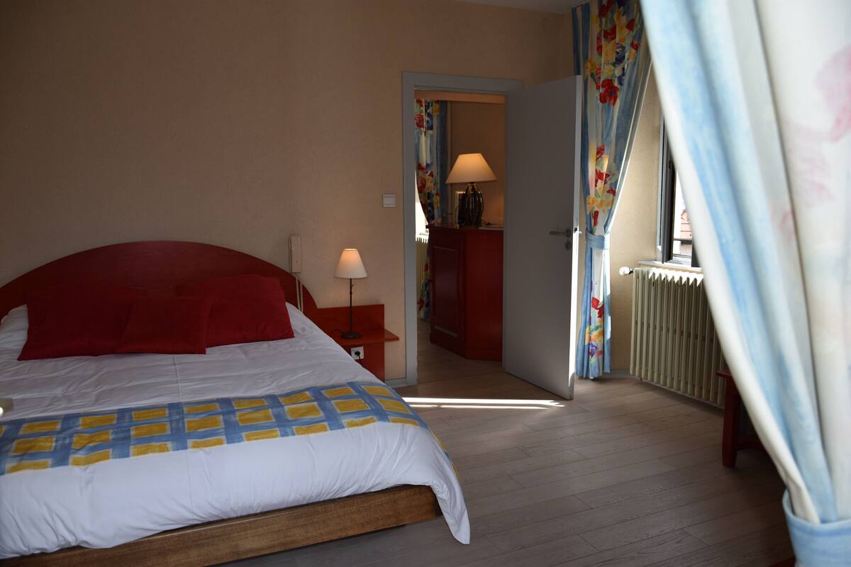 Une chambre à coucher avec un lit, une table de chevet, une lampe et une vue sur un couloir.