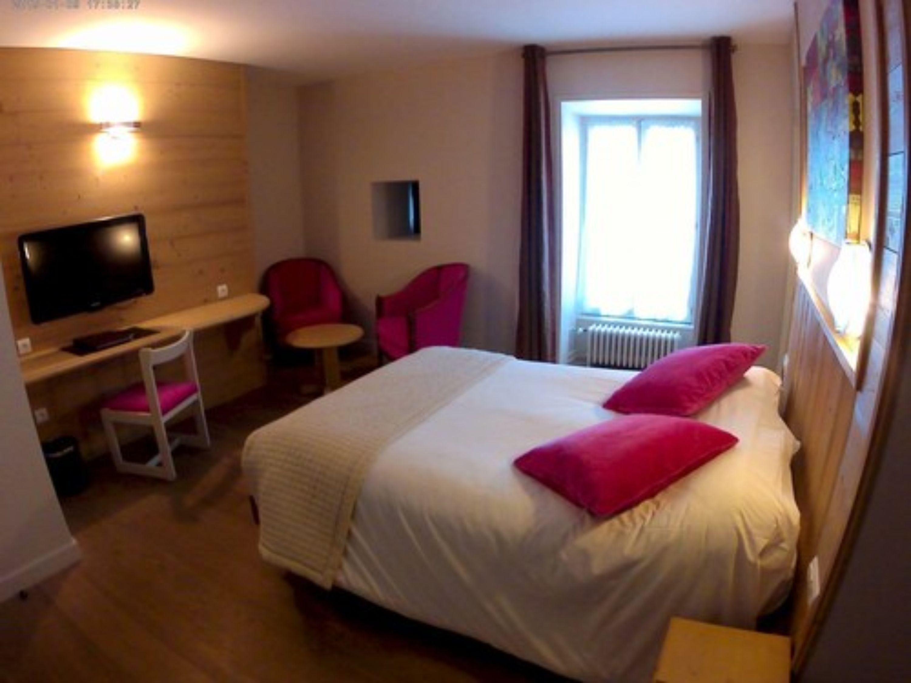 Ein Hotelzimmer mit Bett, Schreibtisch mit Stuhl, Fernseher und einem Fenster mit Vorhängen.