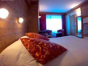 Una habitación de hotel con una cama grande, dos almohadas rojas estampadas, un escritorio con una silla y una ventana con cortinas.