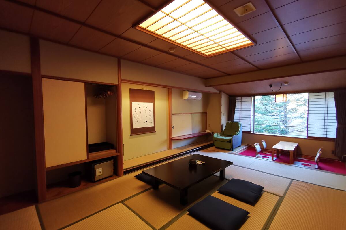 A traditional Japanese room with tatami flooring, a low table, cushions, a chair, and a sliding door.