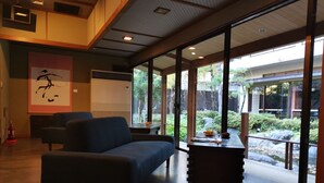 A modern interior with a sofa, a table, and a large window offering a view of a garden.