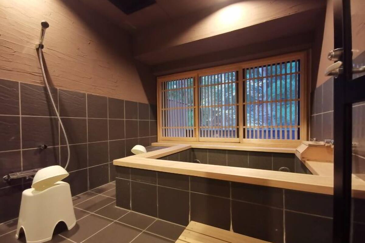 A small bathroom with a bathtub, a window with a view, and a white stool.