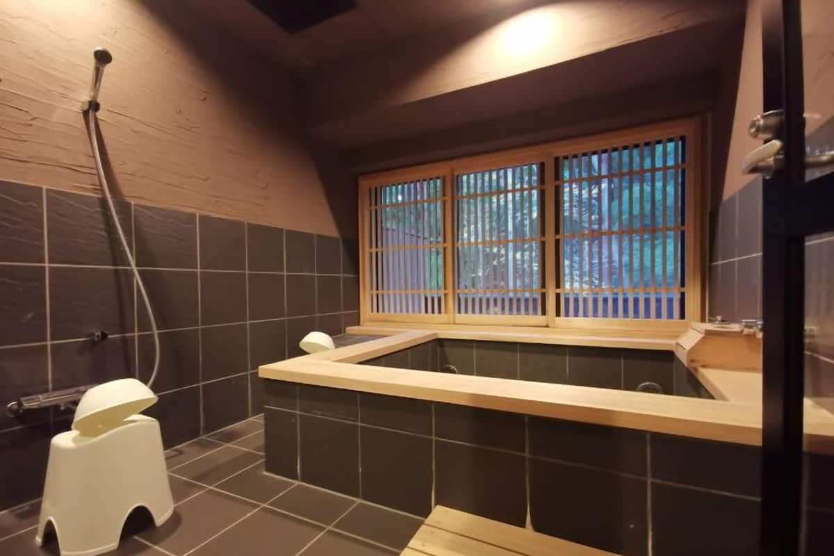 Une petite salle de bain avec une baignoire, une fenêtre donnant sur un beau paysage et un tabouret blanc.