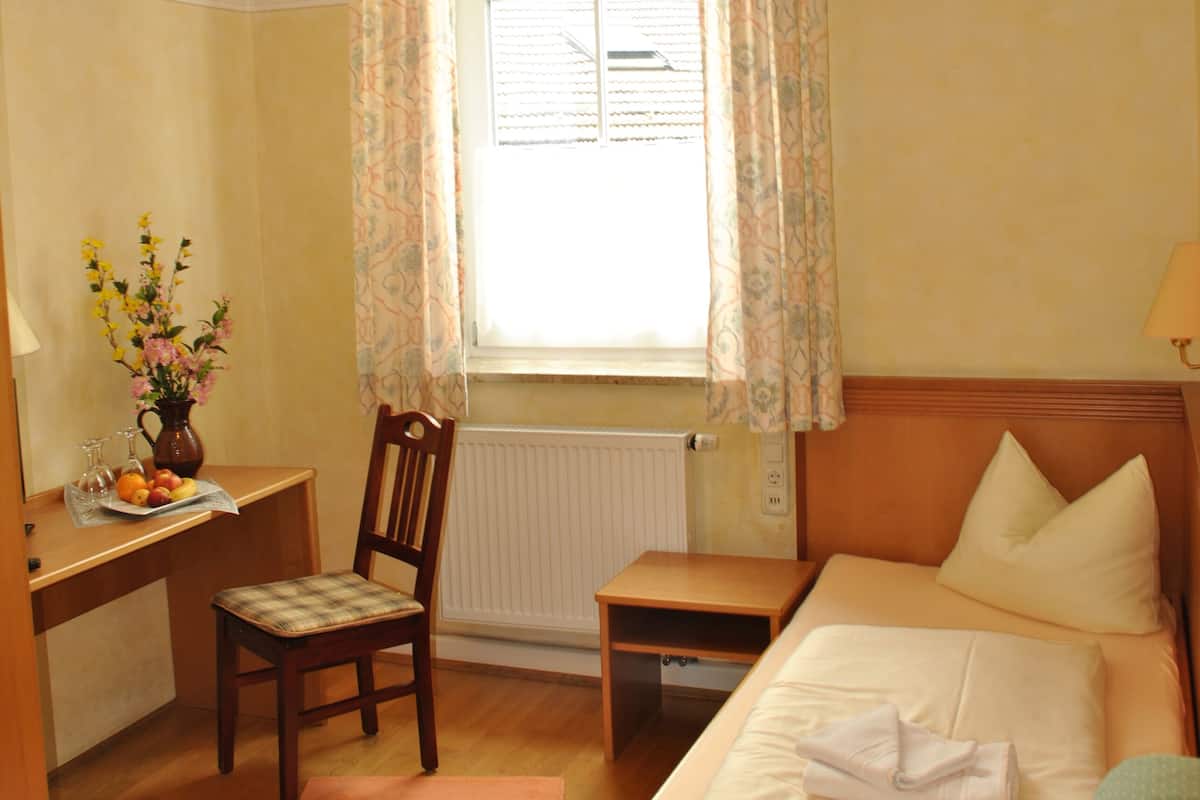 Ein Hotelzimmer mit Bett, Schreibtisch, Stuhl, einem Fenster mit Vorhängen und einem Heizkörper.