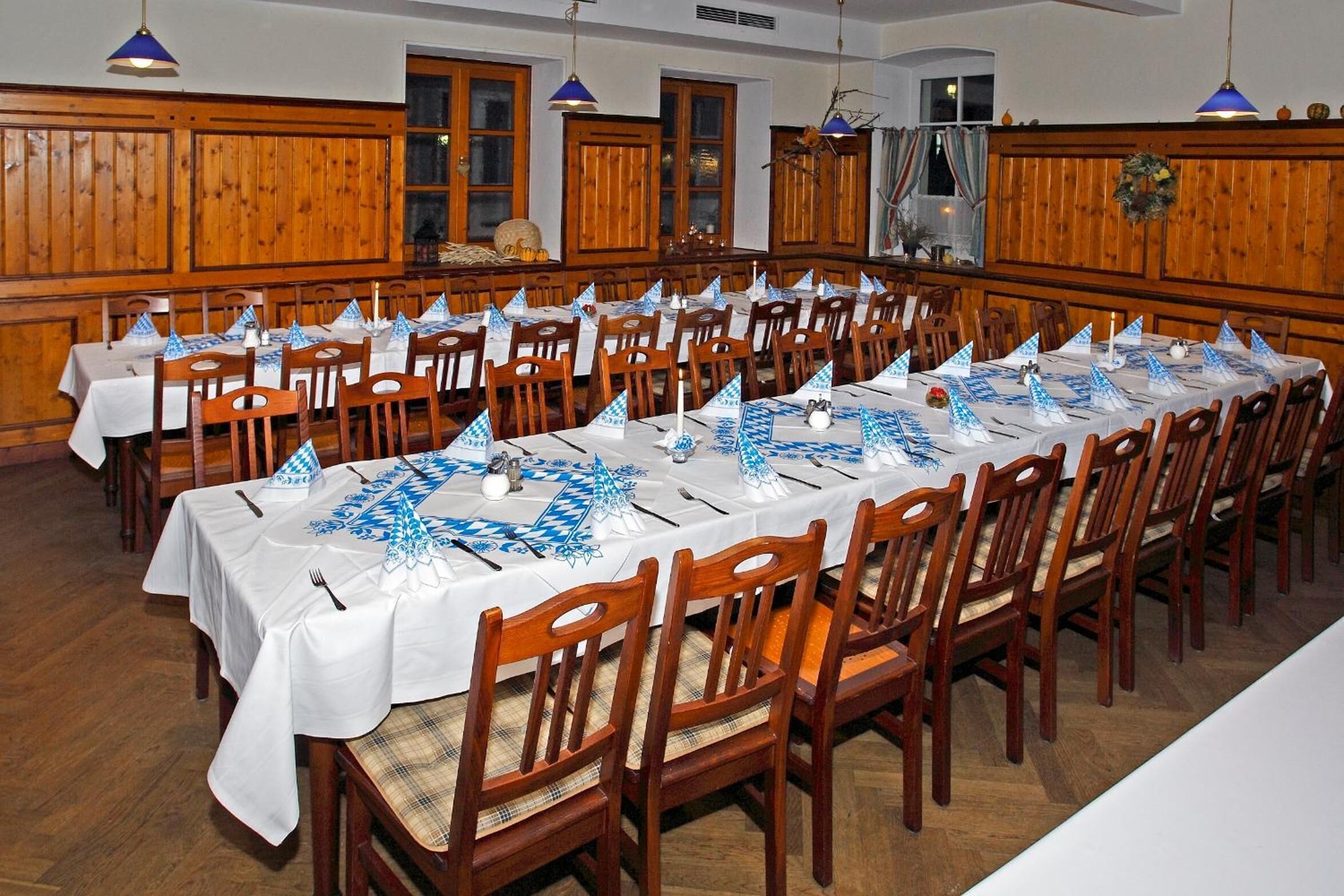 Una larga mesa de comedor dispuesta con sillas, manteles blancos y caminos de mesa azules.