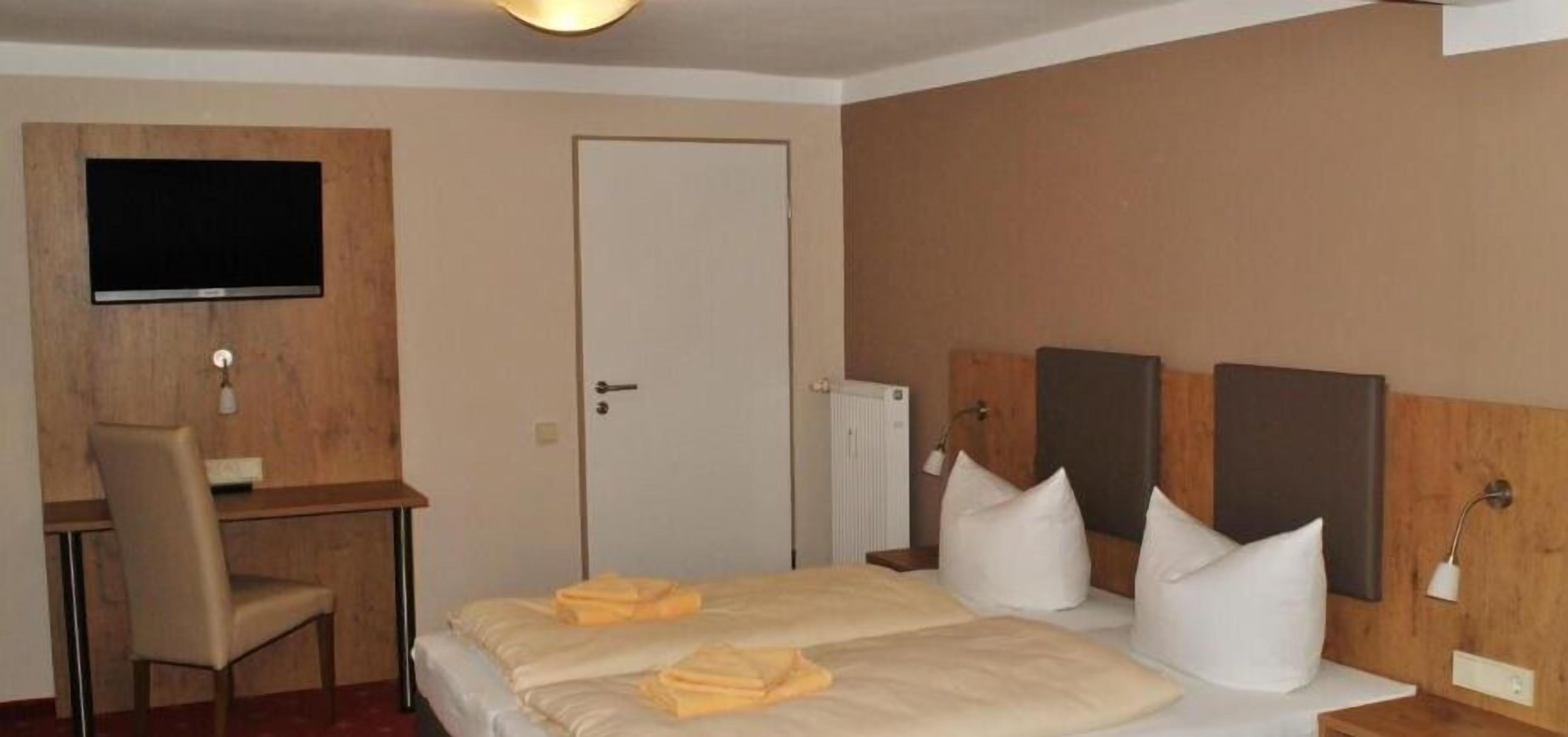 Una habitación de hotel con una cama, un escritorio, una silla, un televisor y una puerta.