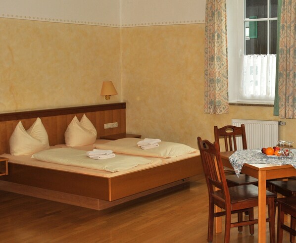 Une chambre d’hôtel avec un lit en bois, une table avec des fruits et une fenêtre avec des rideaux.