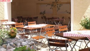 Un espace extérieur aménagé pour les repas, avec des tables et des chaises en bois, un parasol rouge et un lustre.