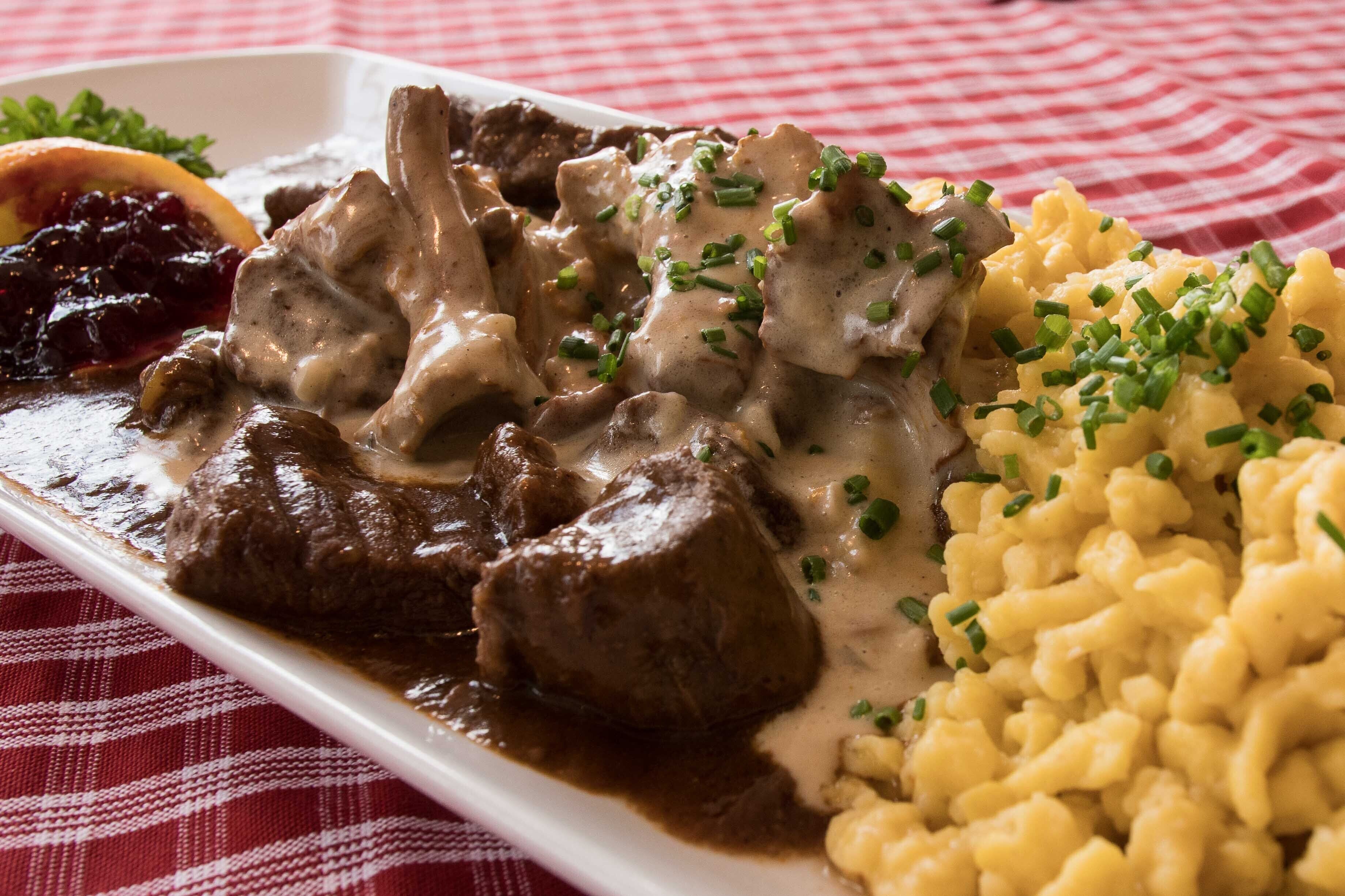 A plate of beef with gravy, mashed potatoes, and cranberry sauce on a checkered tablecloth.