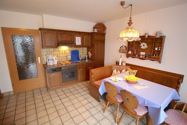 A kitchen with wooden cabinets, a dining table with chairs, a blue tablecloth, and a hanging light fixture. - Carina - Michael - Sissi & Martin (Garmisch-Partenkirchen)
